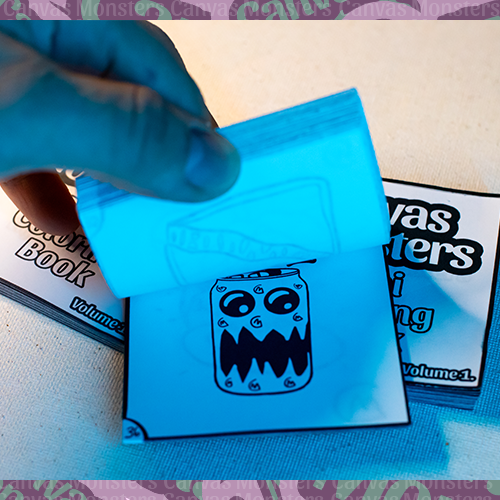 Hand flipping through the Canvas Monsters Mini Coloring Book Volume 1 on a white surface.