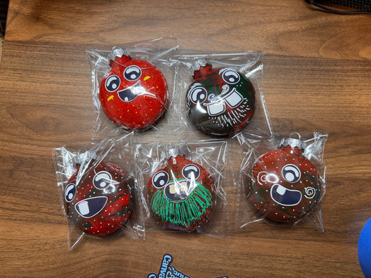 Five Canvas Monsters ornaments in various shades of red with sticker faces on each one.