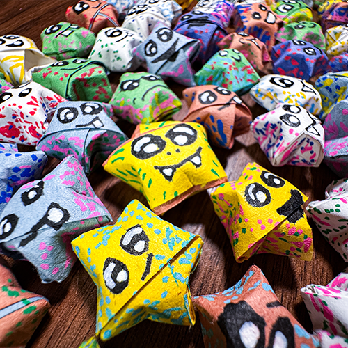 Close up image of origami paper starts of various colors with different faces painted on each one.