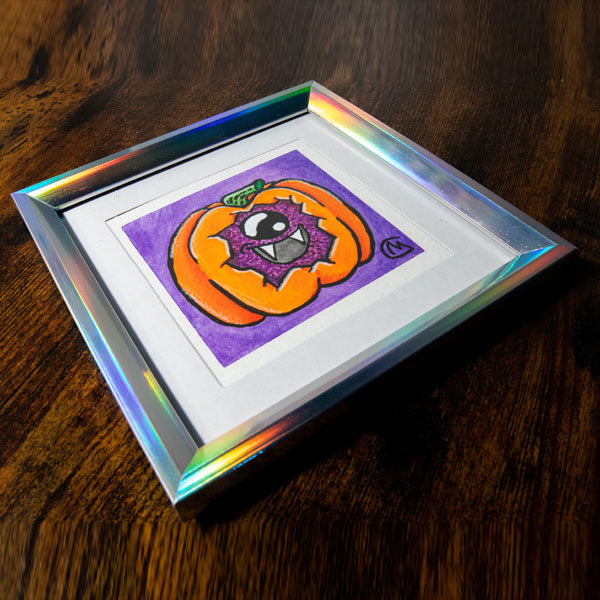 A small, original watercolor painting featuring a cartoon-style pumpkin monster with a smiling face, painted on watercolor paper, framed in a irredenscent frame.