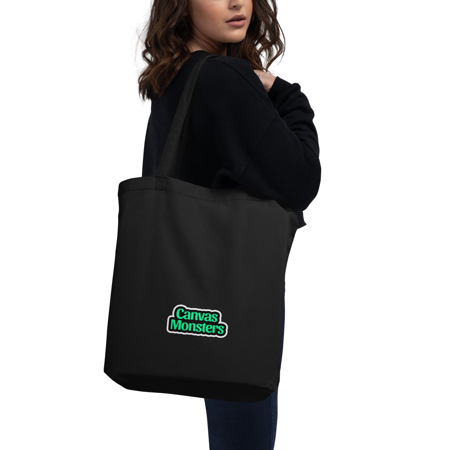 Black tote bag with 'Canvas Monsters' logo held by a person on a white background