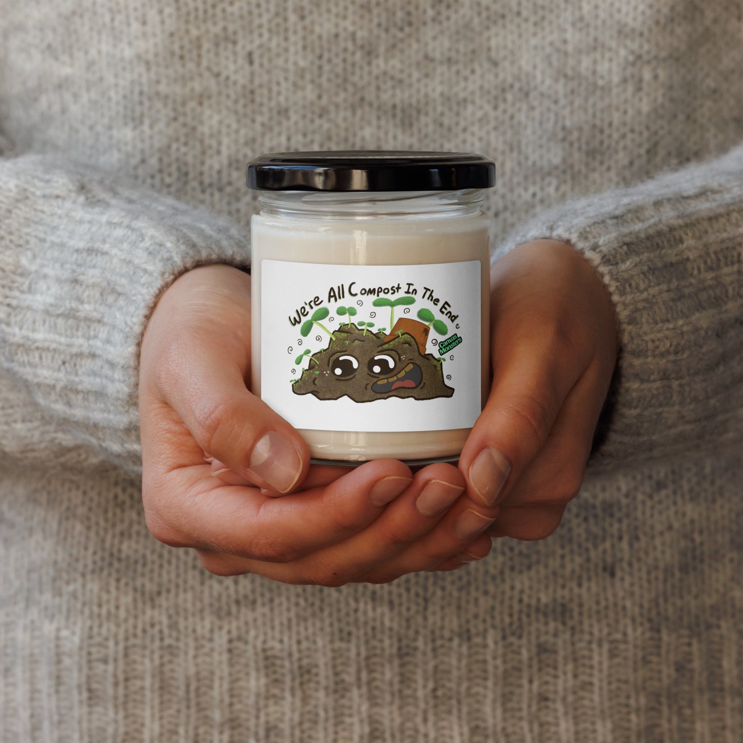 Hands holding a candle with a compost-themed label against a neutral background