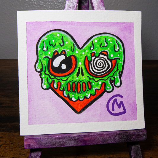 A watercolor painting of a heart-shaped monster with green slime and a purple background, displayed on a mini easel.