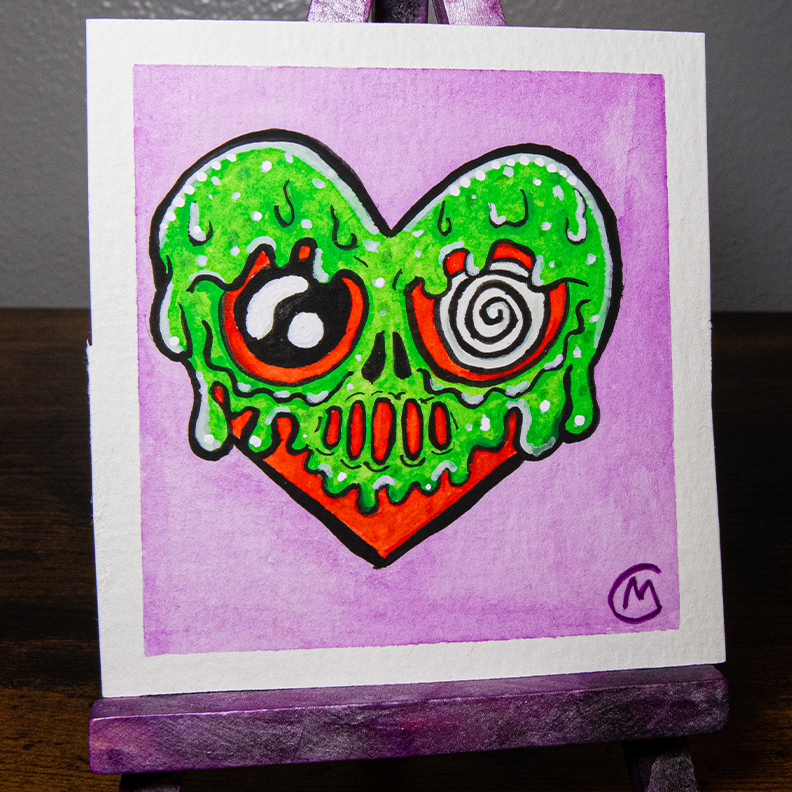 A watercolor painting of a heart-shaped monster with green slime and a purple background, displayed on a mini easel.