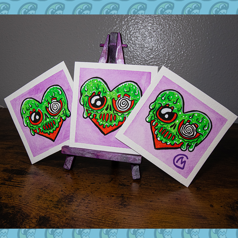 Three watercolor paintings of a heart-shaped monster with green slime and a purple background, displayed on a mini easel.