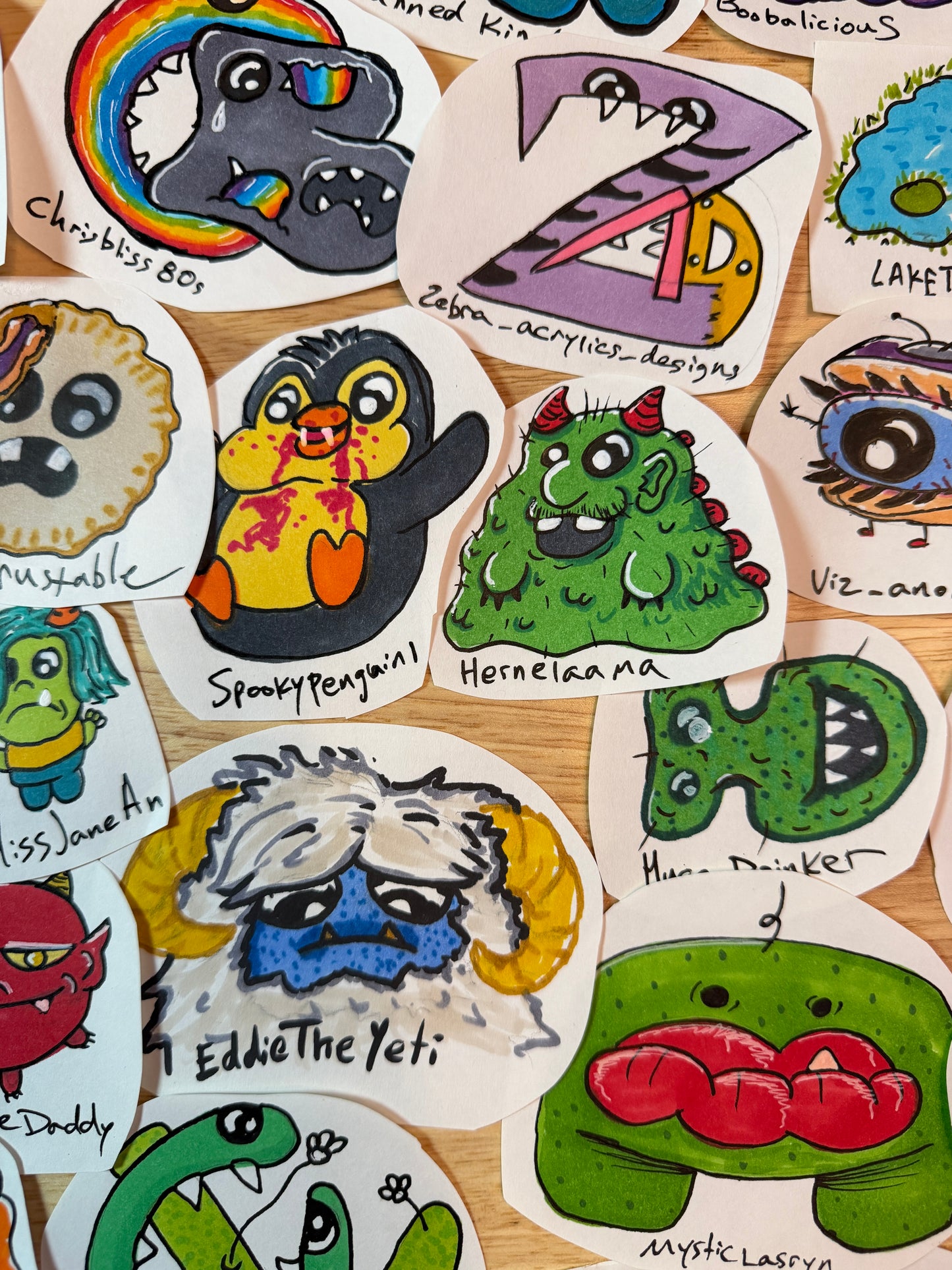 A collection of hand-drawn whimsical monsters, animals, and faces, arranged on a light wood background.