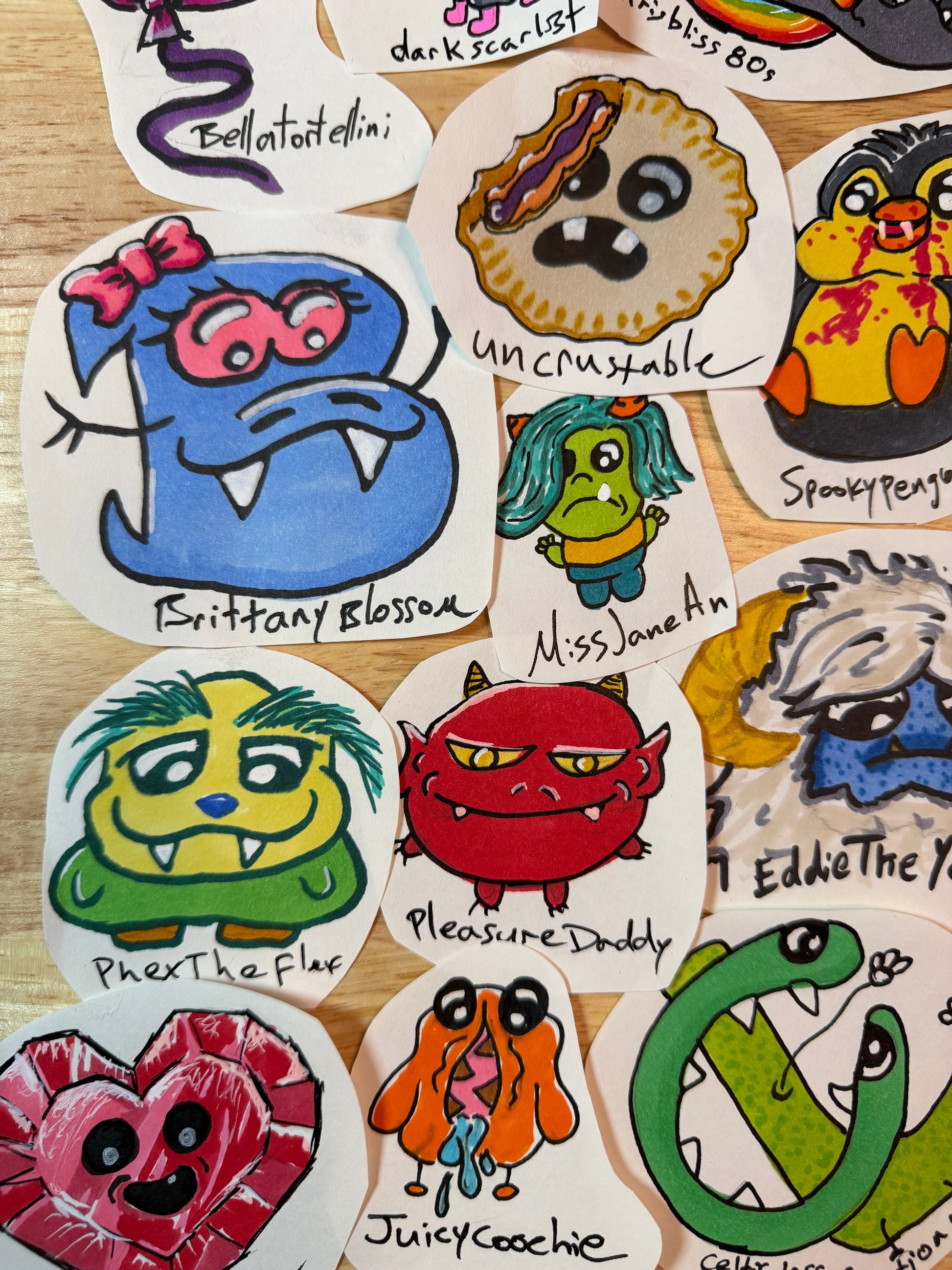 A collection of hand-drawn, die-cut cartoon stickers featuring various colorful monster and character designs, arranged on a light wood surface.