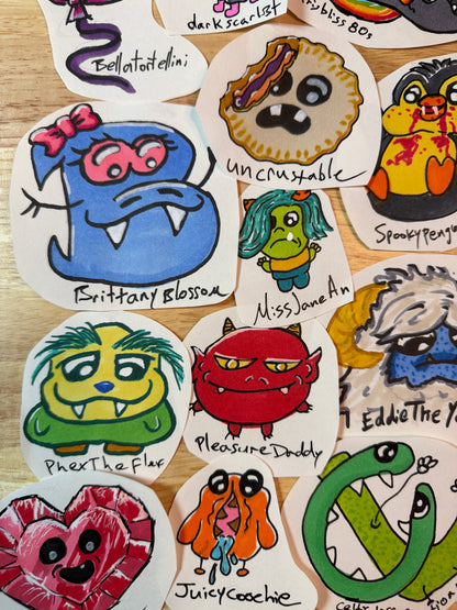 A collection of hand-drawn, die-cut cartoon stickers featuring various colorful monster and character designs, arranged on a light wood surface.
