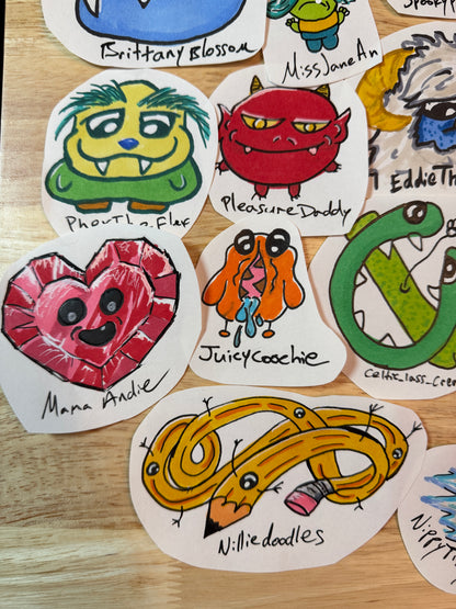 A collection of hand-drawn monster and character stickers arranged on a light wood surface. The stickers feature colorful cartoon designs including a green monster, a red demon, a pink heart, an orange dog, a yellow coiled snake, and others, each labeled with a playful name.