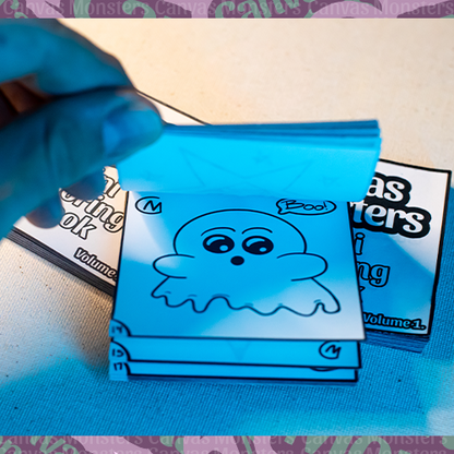 Hand flipping through the Canvas Monsters Mini Coloring Book Volume 1 on a white surface. Photo shown is a cartoon ghost.