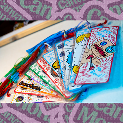 Colorful painted bookmarks with Canvas Monsters designs on a white surface.