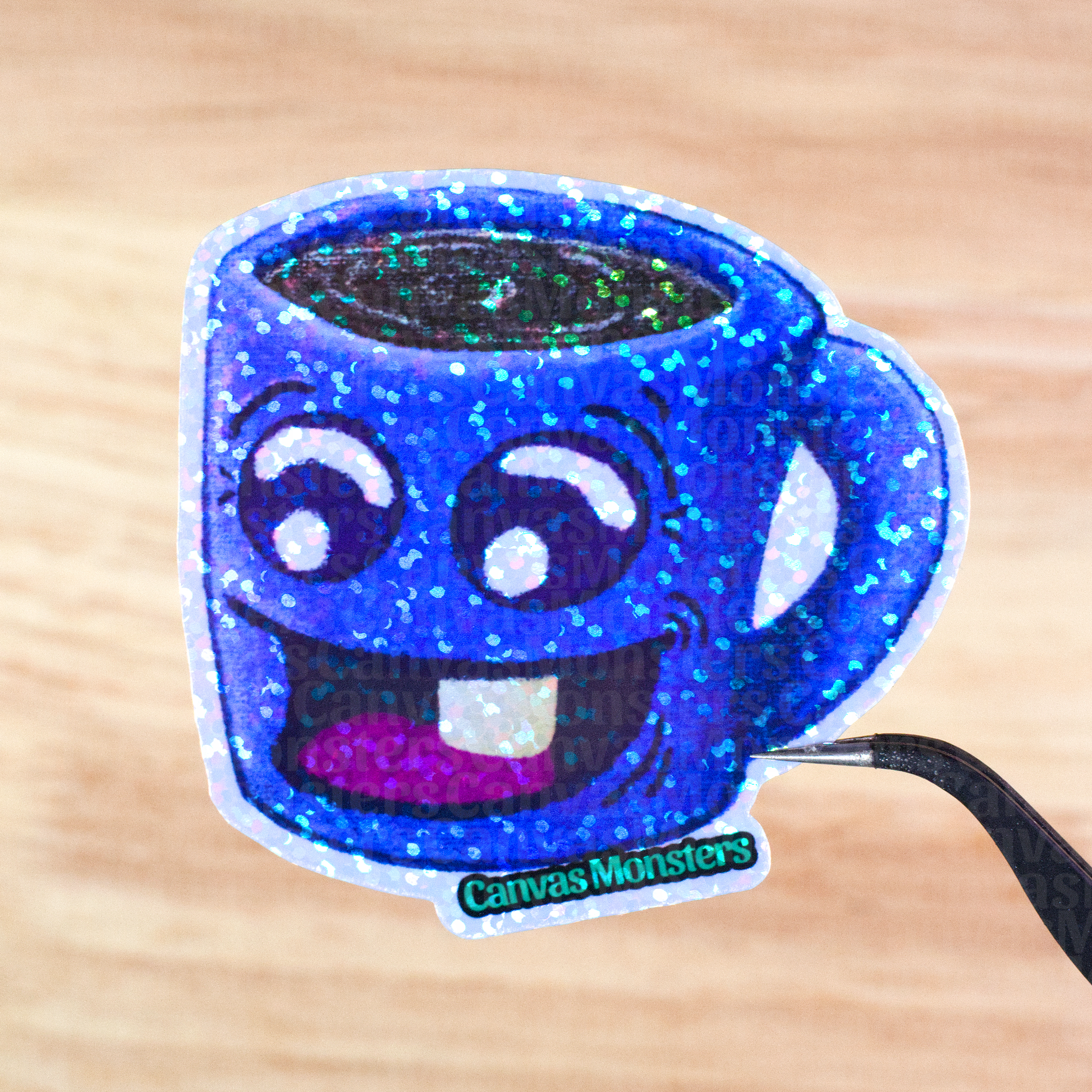 Glittery sticker of a blue mug with a happy face held above a wooden surface, branded 'Canvas Monsters'.