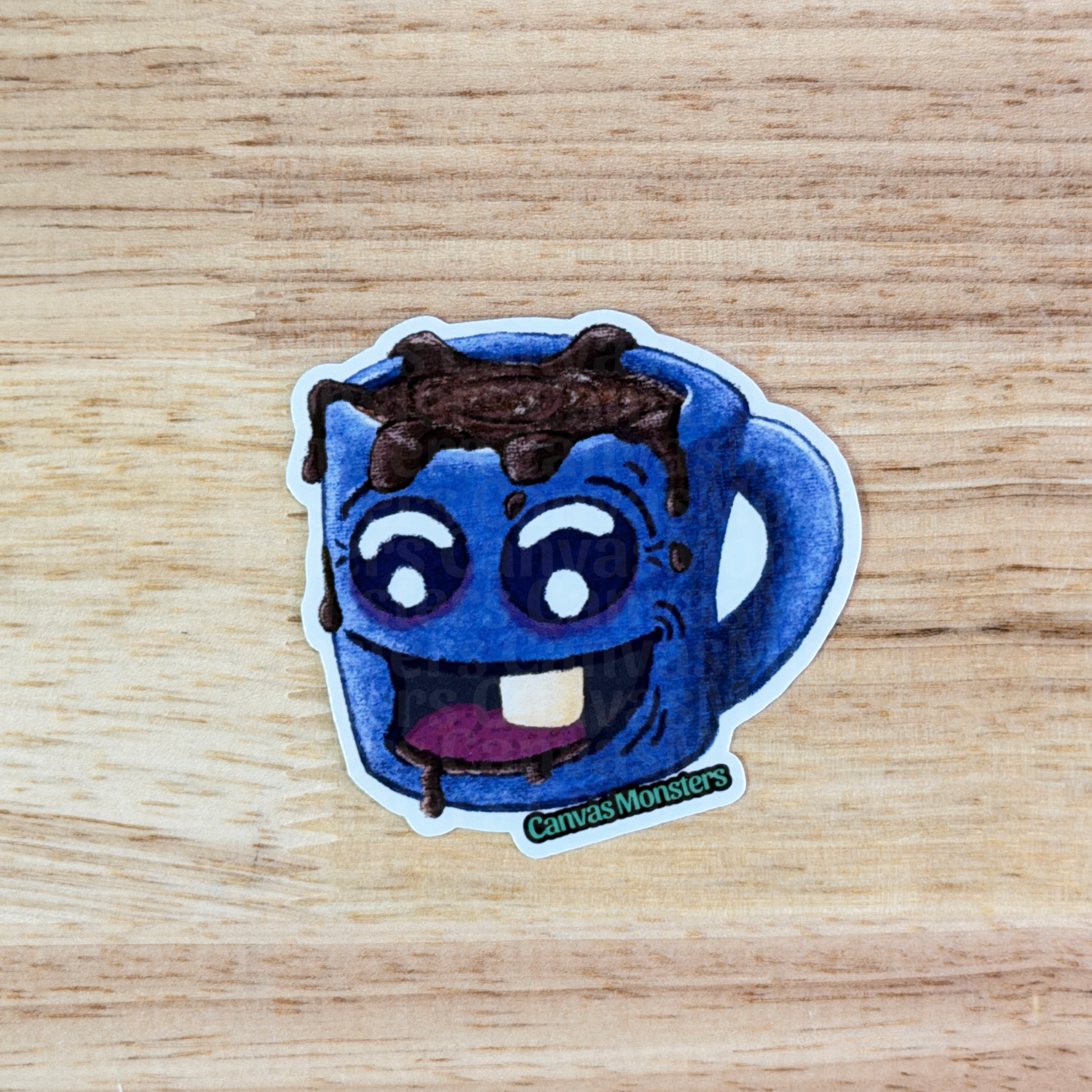 Sticker of a blue creature with coffee spilling out, sitting on a wooden surface.