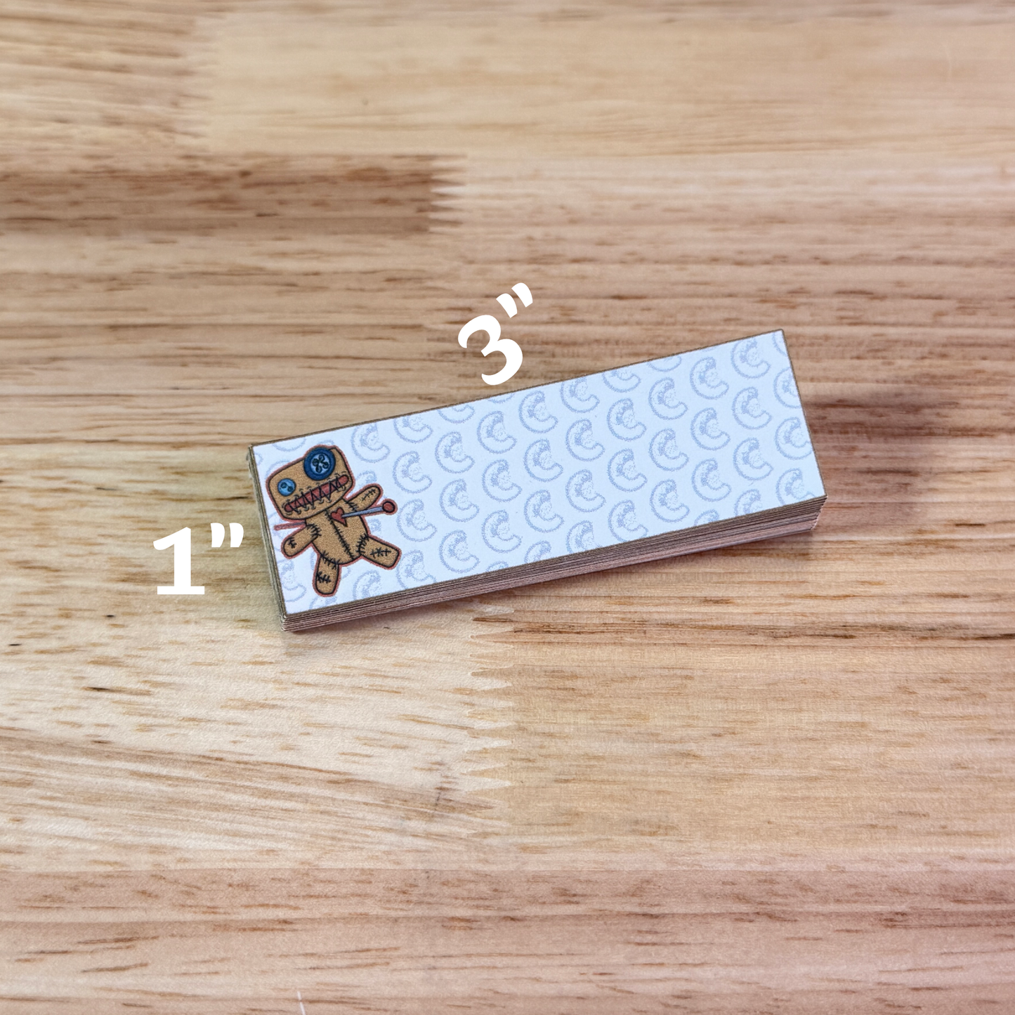 1" by 3" sticky notepad with an illustration of a cartoon voodoo doll