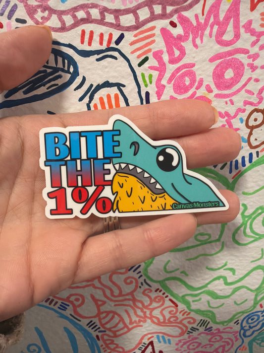 A hand holding a die-cut sticker featuring a cartoon shark and the text 'BITE THE 1%'. The sticker has a white border and is shown against a colorful, patterned background.
