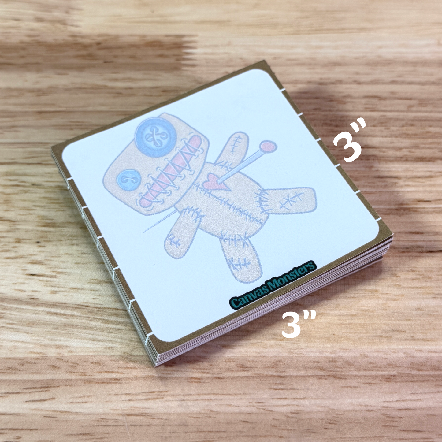 Small sticky notepad with a voodoo doll illustration, sitting on a wooden surface