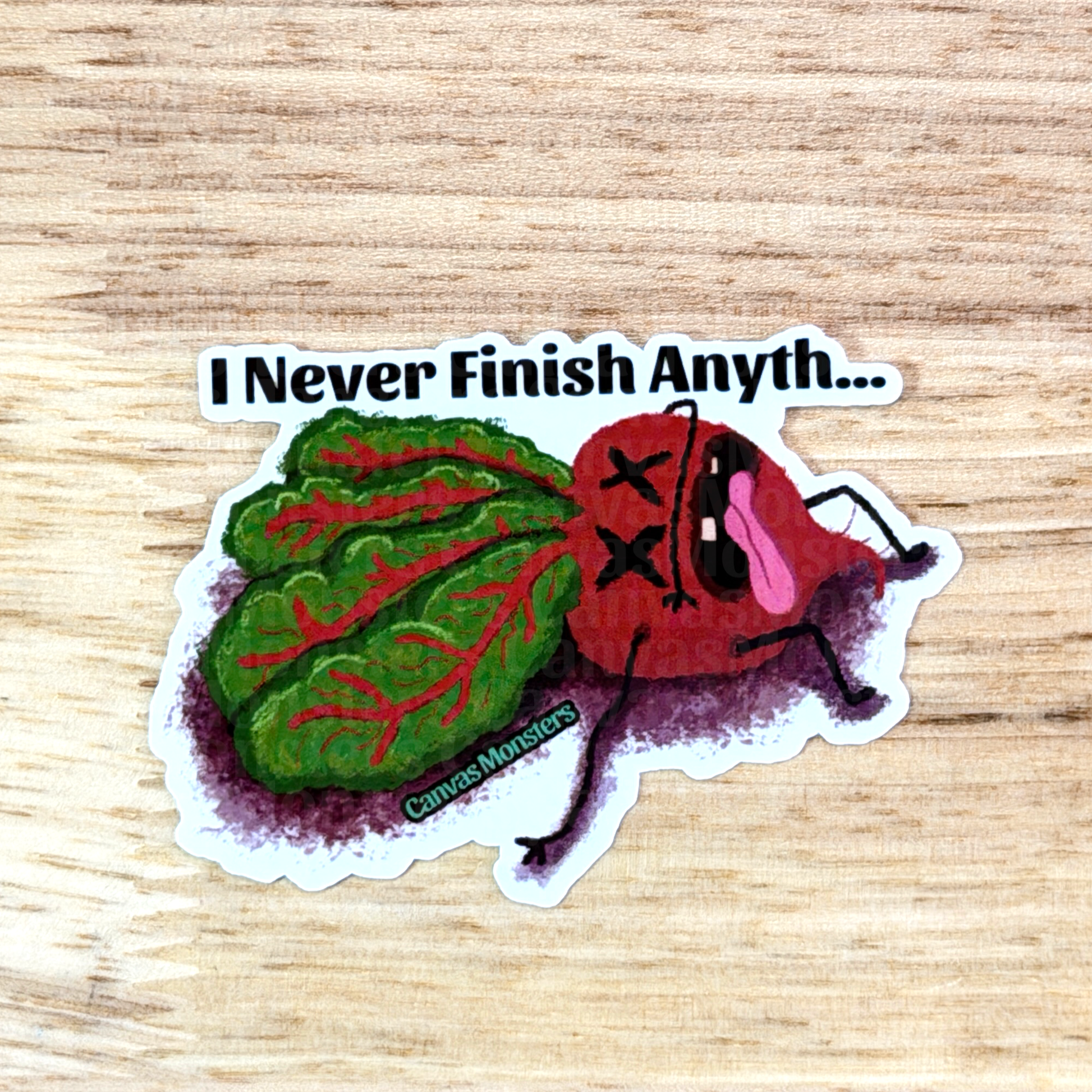 Sticker with a cartoon characterized beet and text 'I Never Finish Anyth...' on a wooden surface