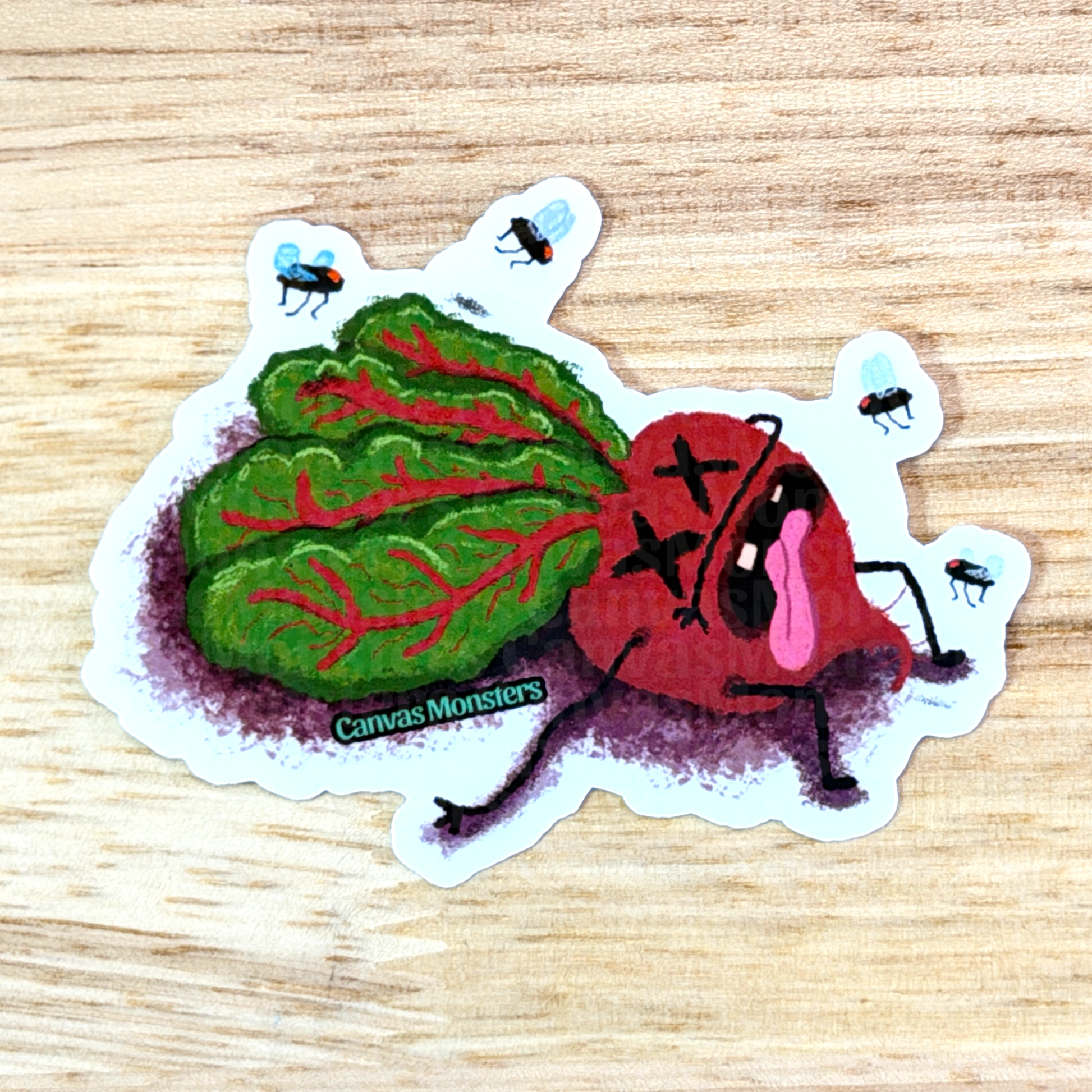 Sticker of a red and green beet creature with 'Canvas Monsters' branding on a wooden surface.