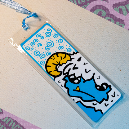 White paper bookmark with Canvas Monsters character "Eddie the Yeti" painted on it with a blue swirl background and border, in a plastic sleeve and matching blue tassel.