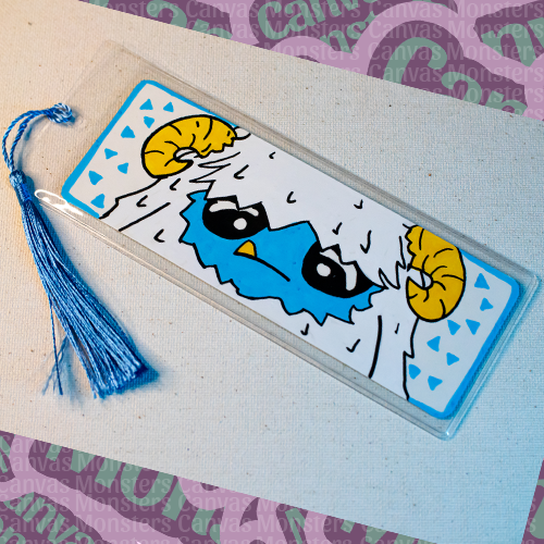 White paper bookmark with Canvas Monsters character "Eddie the Yeti" painted on it with small blue triangles in the background and a blue border, in a plastic sleeve and matching blue tassel.