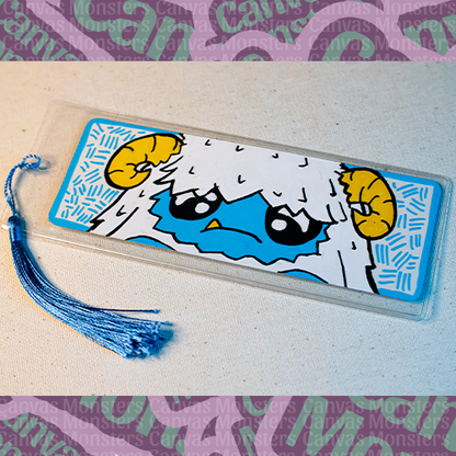 White paper bookmark with Canvas Monsters character "Eddie the Yeti" painted on it with a blue hash mark background and border, in a plastic sleeve and matching blue tassel.