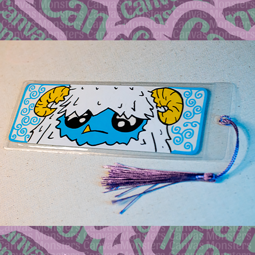 White paper bookmark with Canvas Monsters character "Eddie the Yeti" painted on it with a blue swirl background and border, in a plastic sleeve and matching blue and purple tassel.