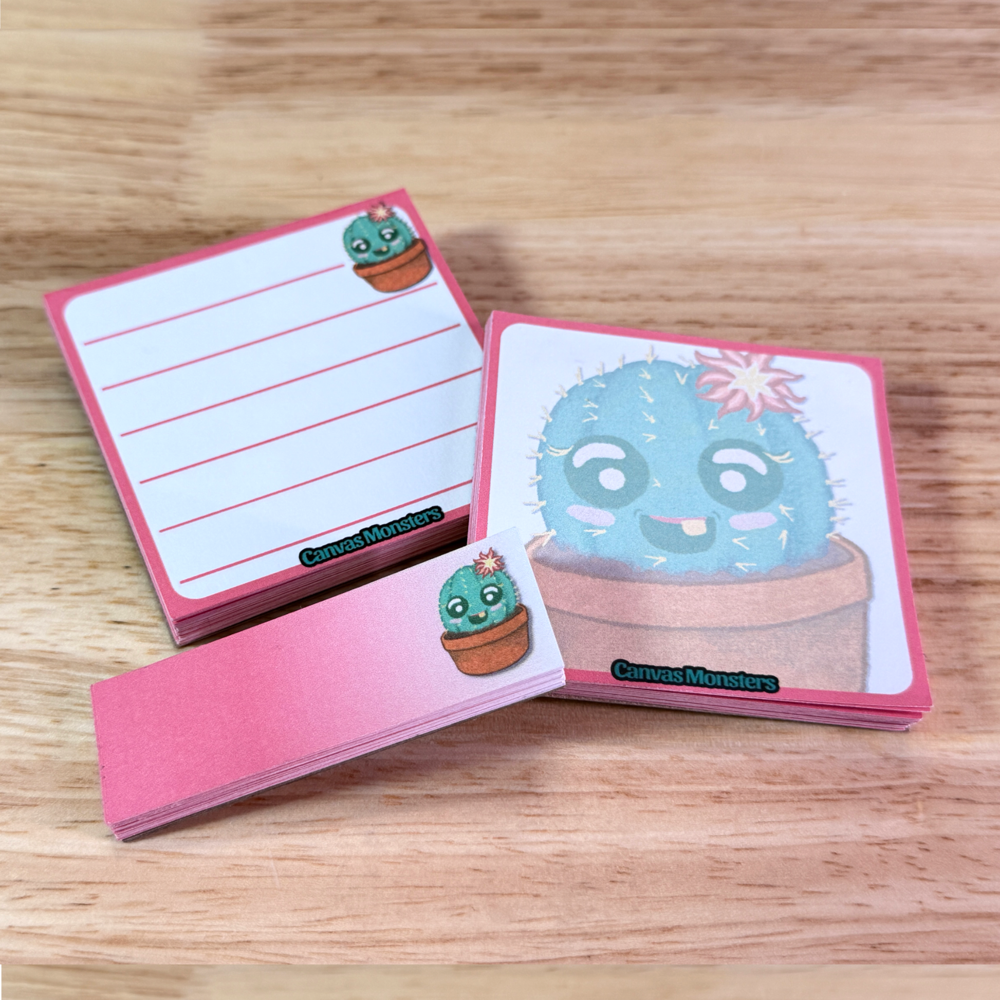 Full set of stationary, including a 3x3 memo pad, a 3x3 sticky notepad, and a 1x3 sticky notepad. Each with an illustration of a cartoon cactus, all sitting on a wooden surface.