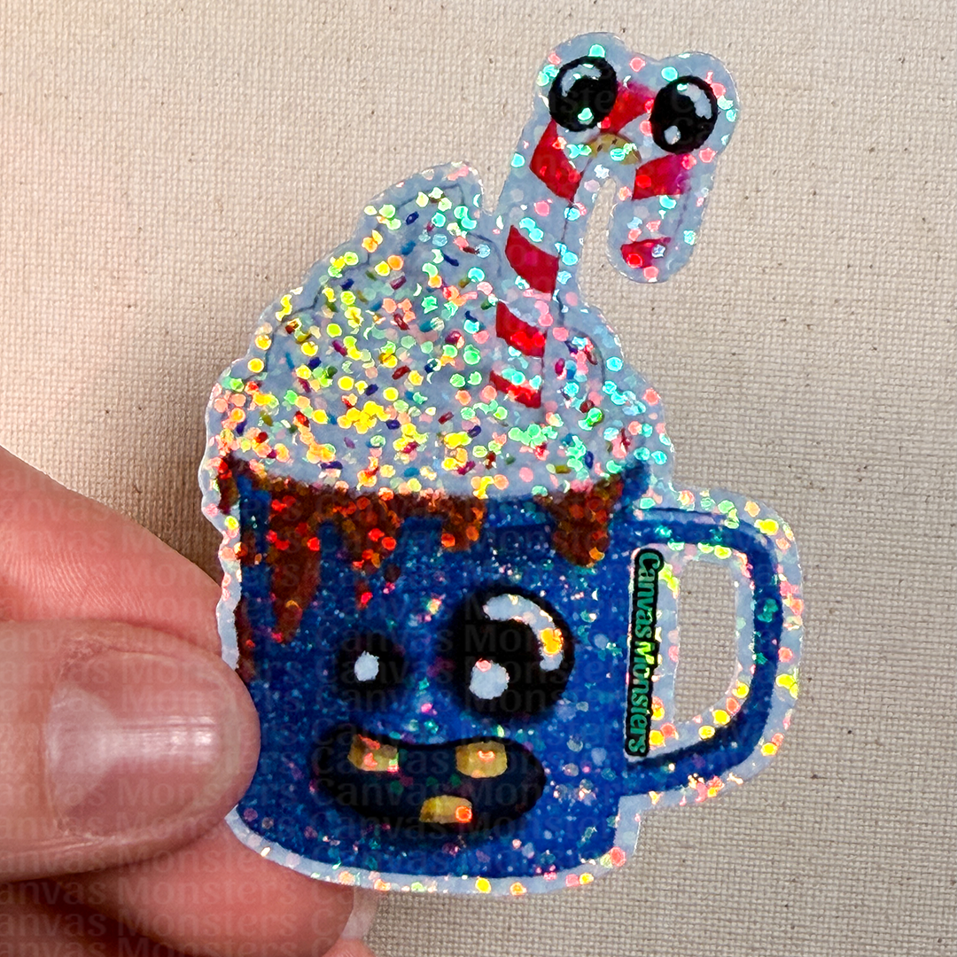 Glittery blue mug with whipped cream and candy cane held by a hand on a beige background