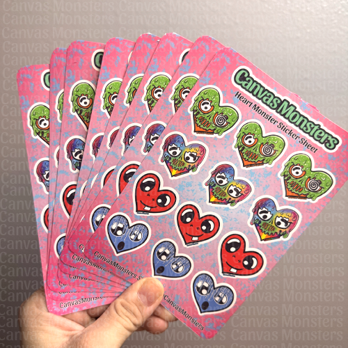Hand holding eight sticker sheets with heart-shaped Canvas Monsters on a neutral background.