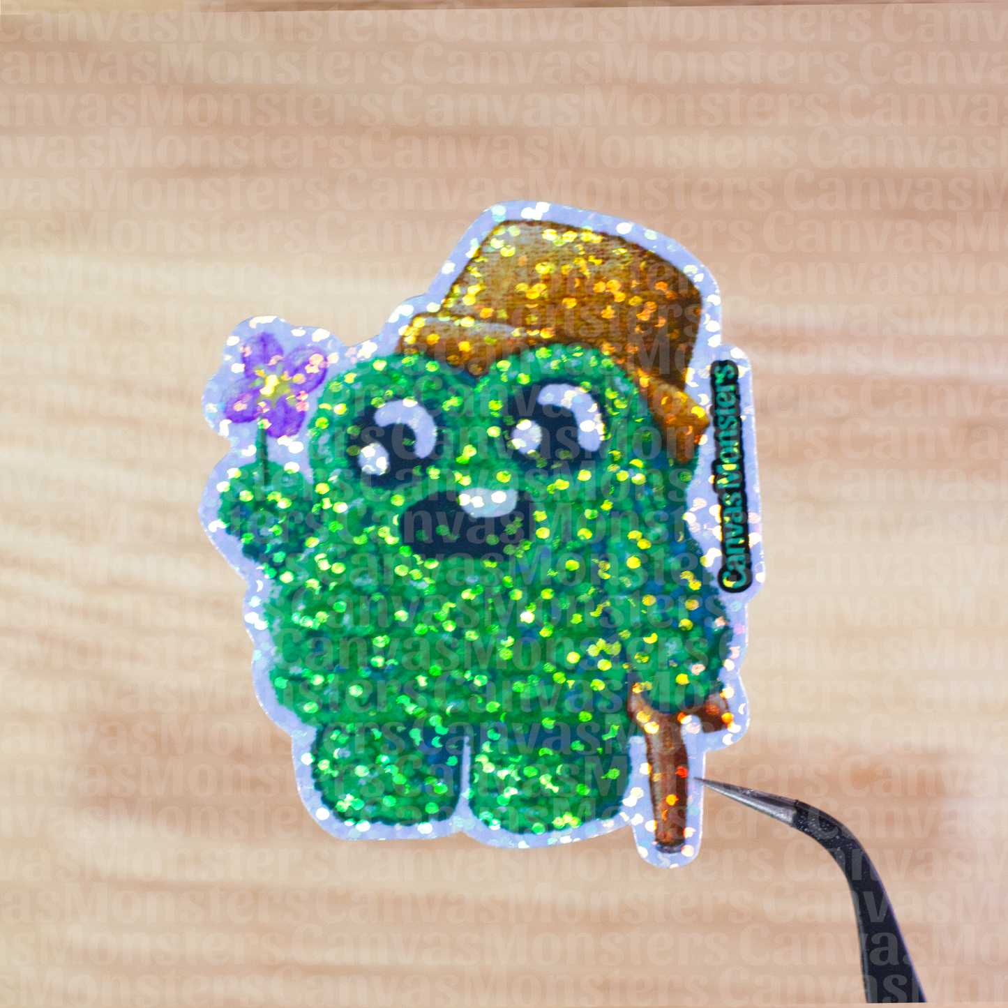 Glitter sticker of a green shrub creature wearing a brown pot as a hat and holding a flower on a wooden surface