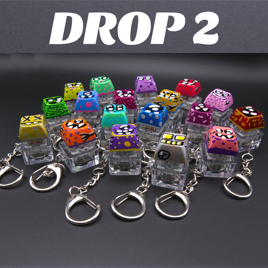 A set of colorful acrylic keychains with cartoon monster faces, arranged on a dark gray background with a 'DROP 2' banner at the top.