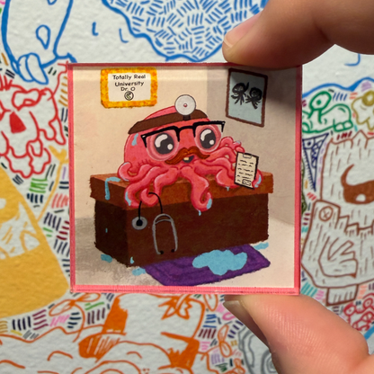 A hand holds a small square magnet featuring a pink octopus dressed as a doctor behind a desk, with the text 'Totally Real University' and 'Class dismissed' visible. The background is a colorful patterned surface.