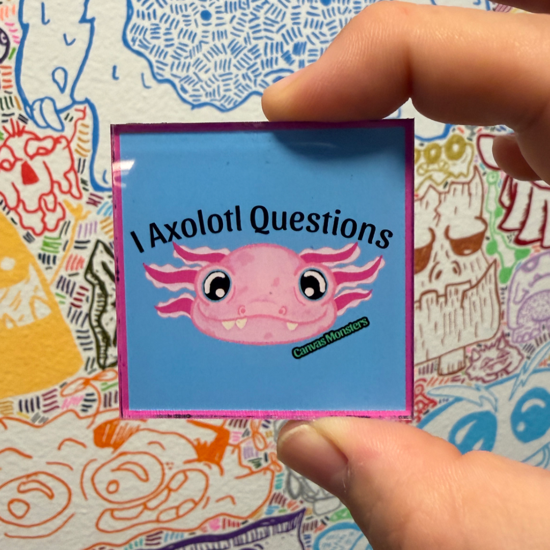 A hand holds a square magnet featuring a pink axolotl on a light blue background with the text 'I Axolotl Questions'. The magnet has a pink border, set against a busy, patterned background.
