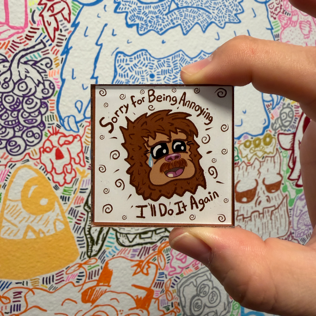 A hand holds a square magnet featuring a cartoon crying sasquatch character with the text 'Sorry for Being Annoying, I'll Do It Again' against a colorful illustrated background.