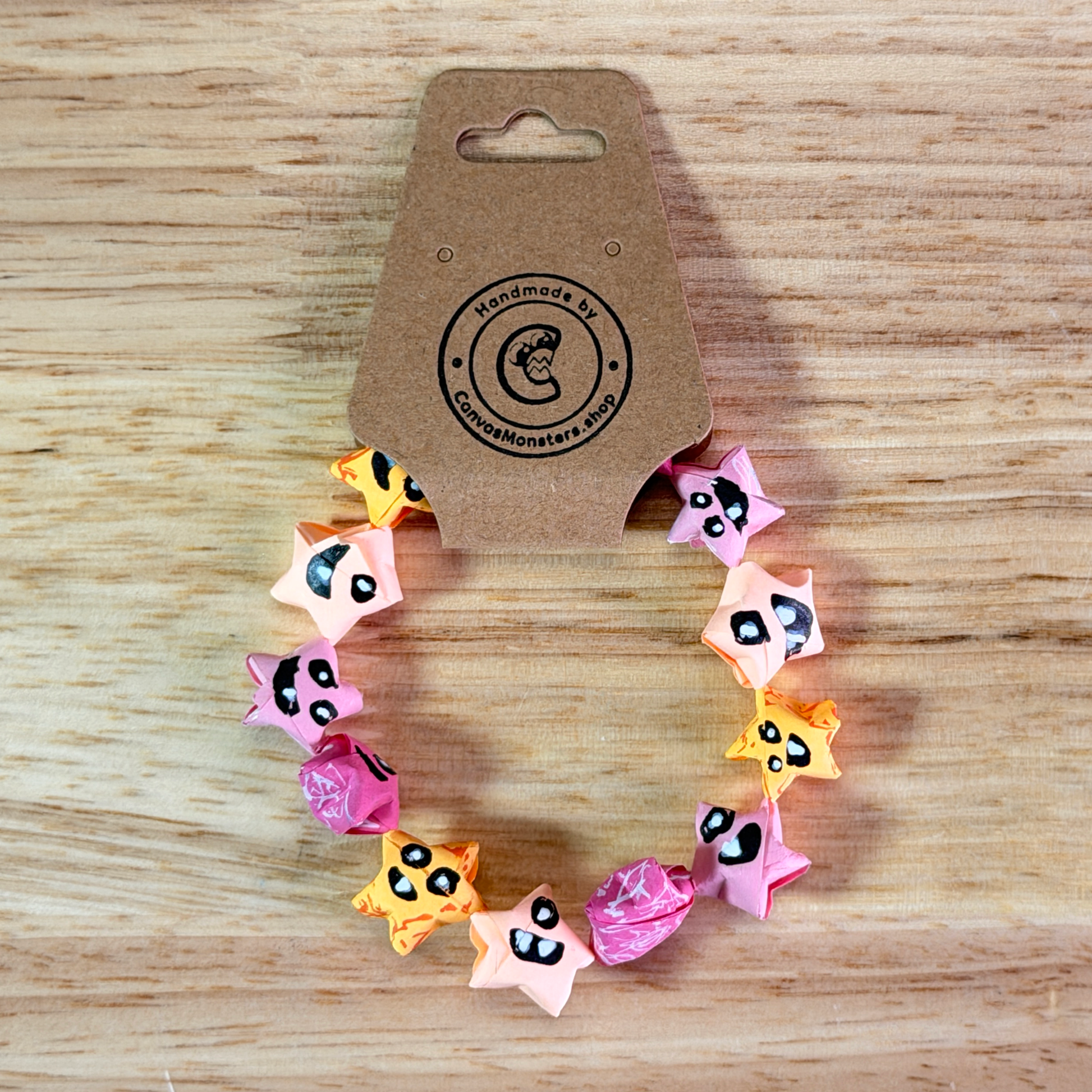 Bracelet with a gradiant of pink, orange, and yellow paper origami star-shaped charms on a wooden background