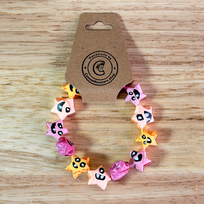 Bracelet with a gradiant of pink, orange, and yellow paper origami star-shaped charms on a wooden background
