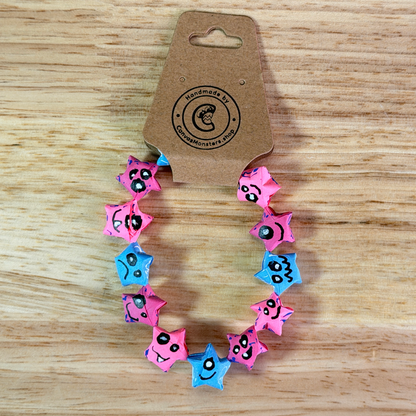 Bracelet with alternating pink and blue paper origami star-shaped charms on a wooden background