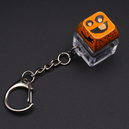 Photo of a key cap keychain on a black background. Cap is painted with an orange monster character.