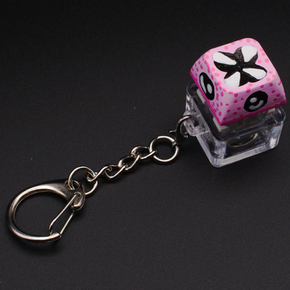Photo of a key cap keychain on a black background. Cap is painted with a pink monster character.