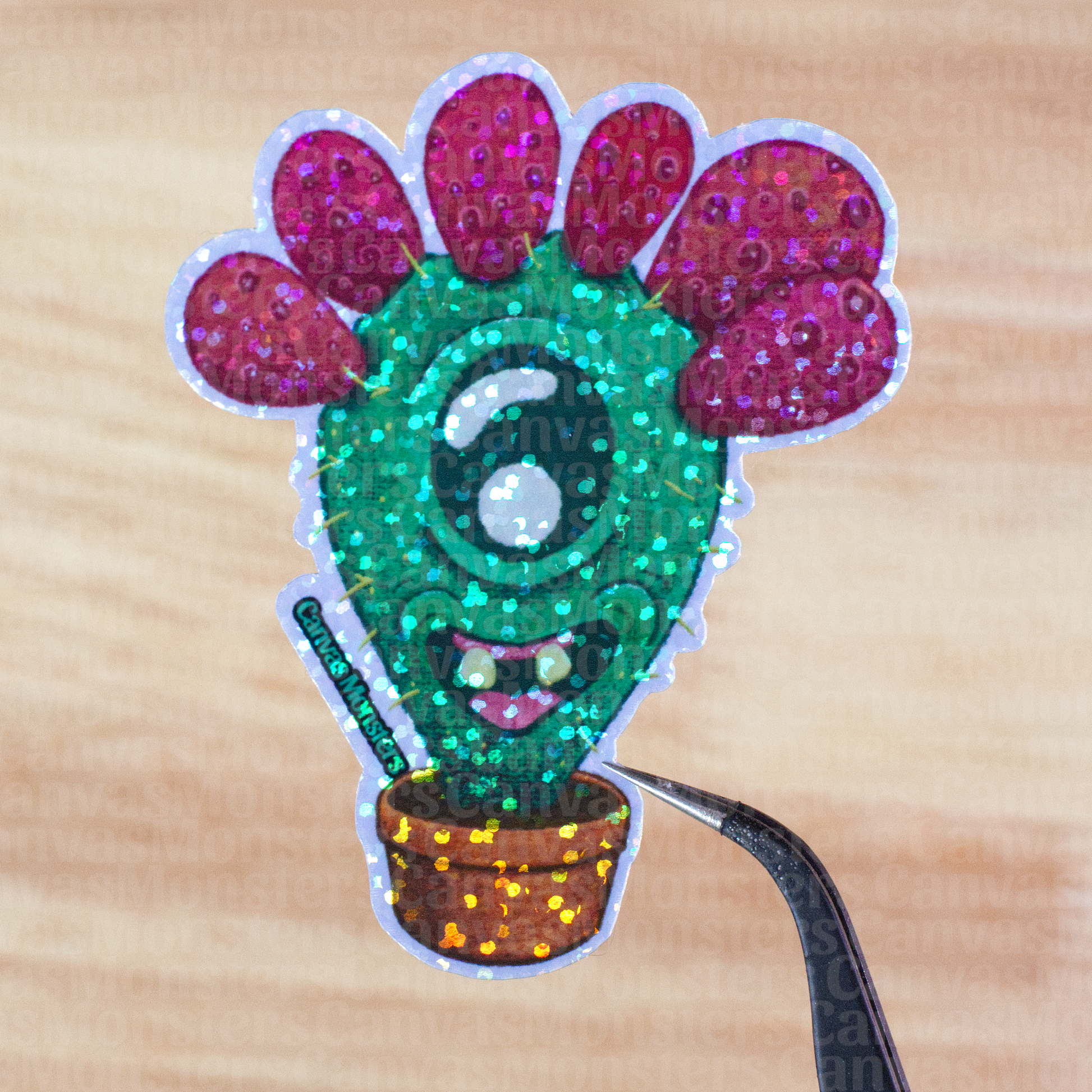 Glitter sticker of a cactus character with red pears, held above a wooden surface