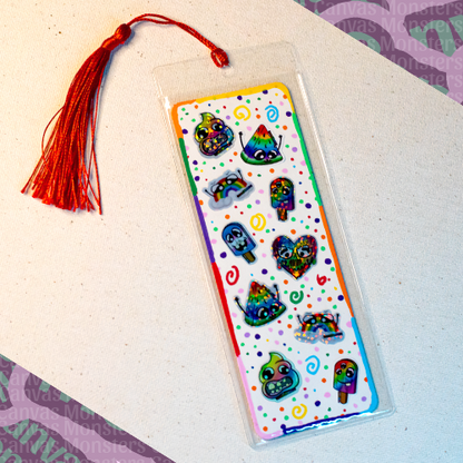 White paper bookmark with mini Canvas Monsters Pride stickers with a colorful painted background of swirls and dots, a colorful border, in a plastic sleeve and red tassel.