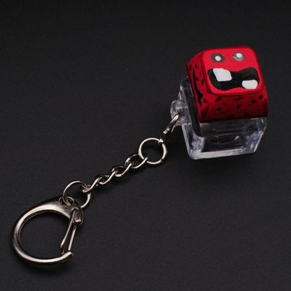 Photo of a key cap keychain on a black background. Cap is painted with a red monster character.