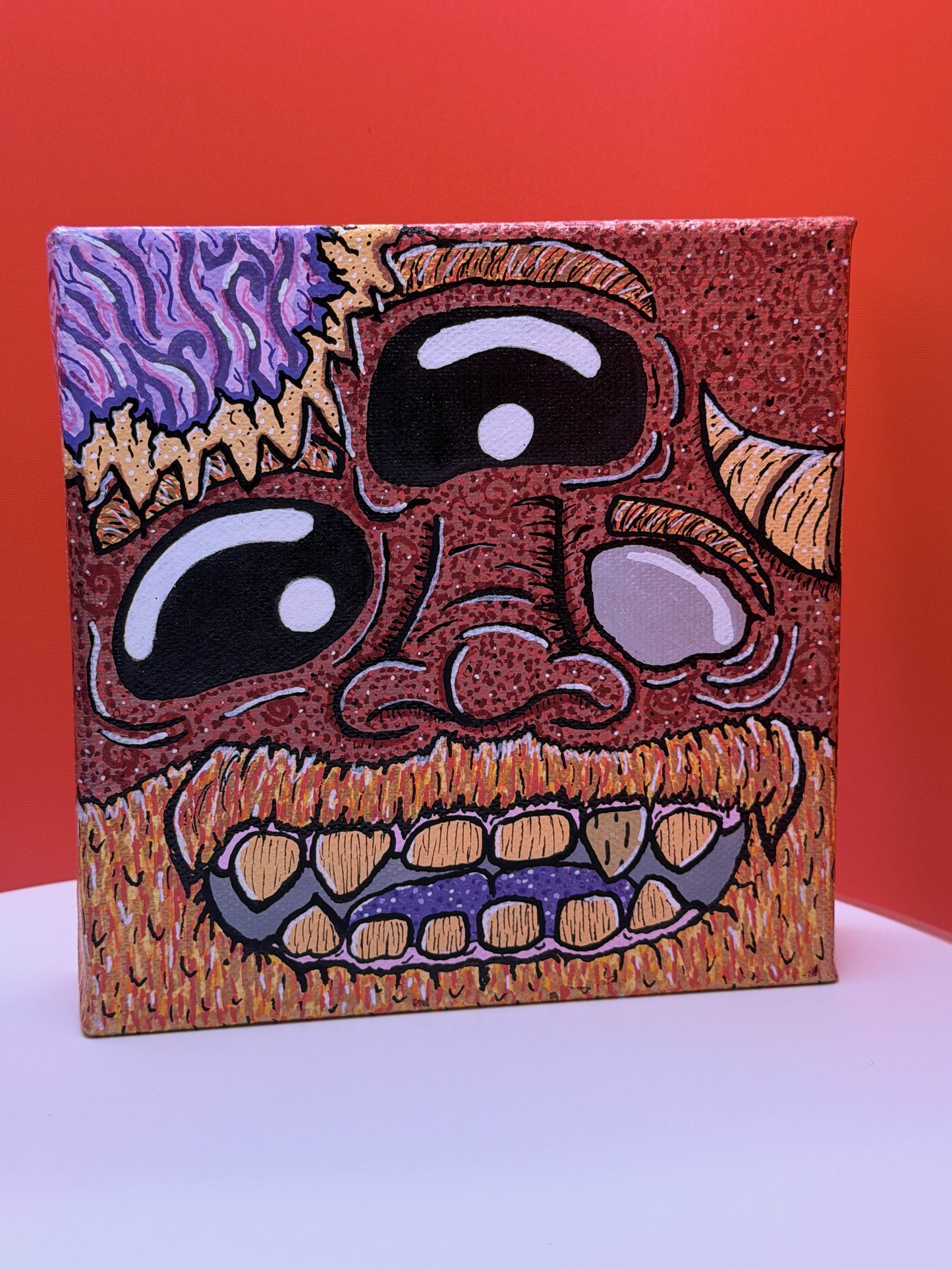 Red and gold monster character painted on a canvas block with purple brains on a red and white background.