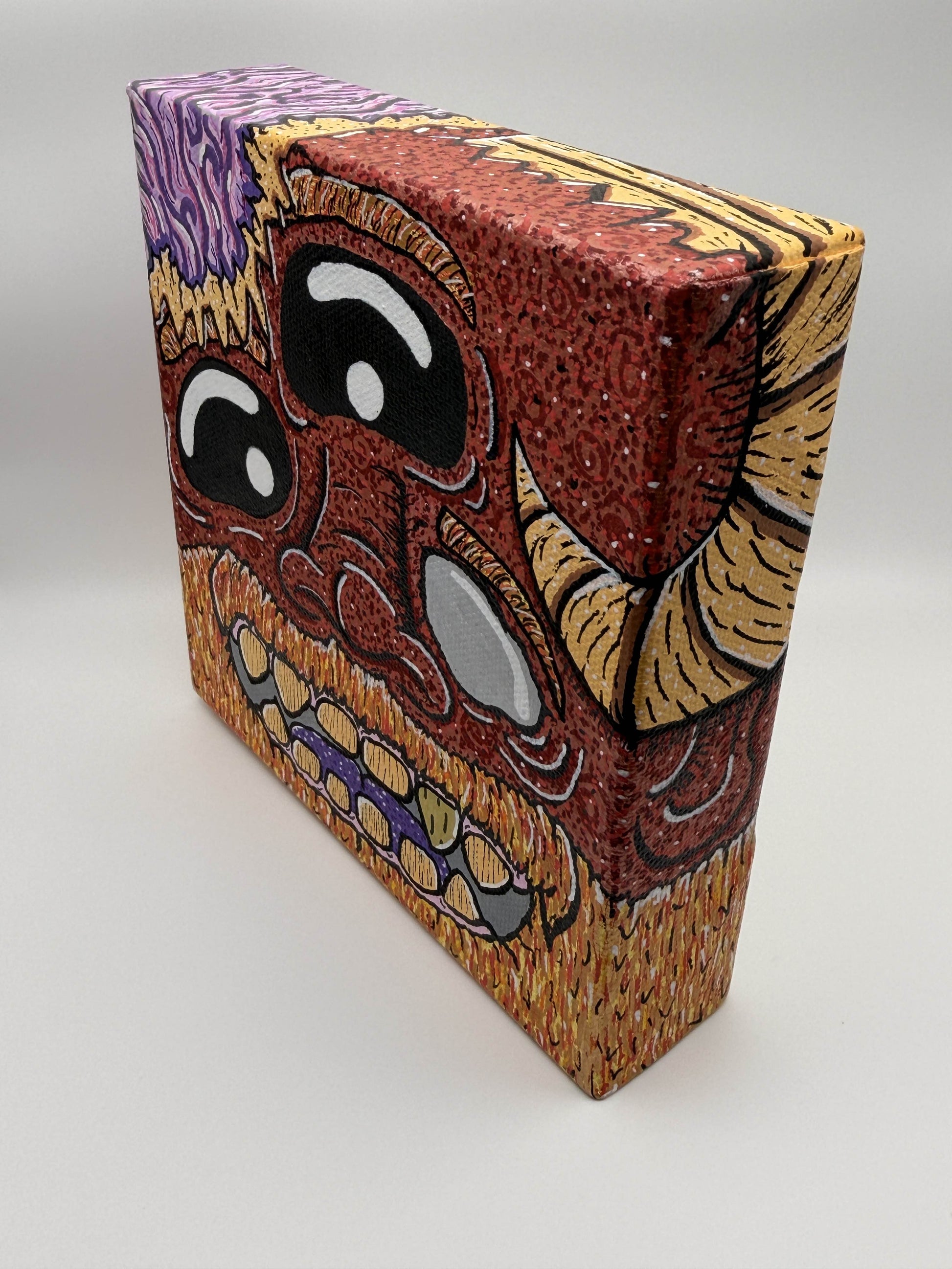 Red and gold monster character painted on a canvas block with purple brains on a white background.