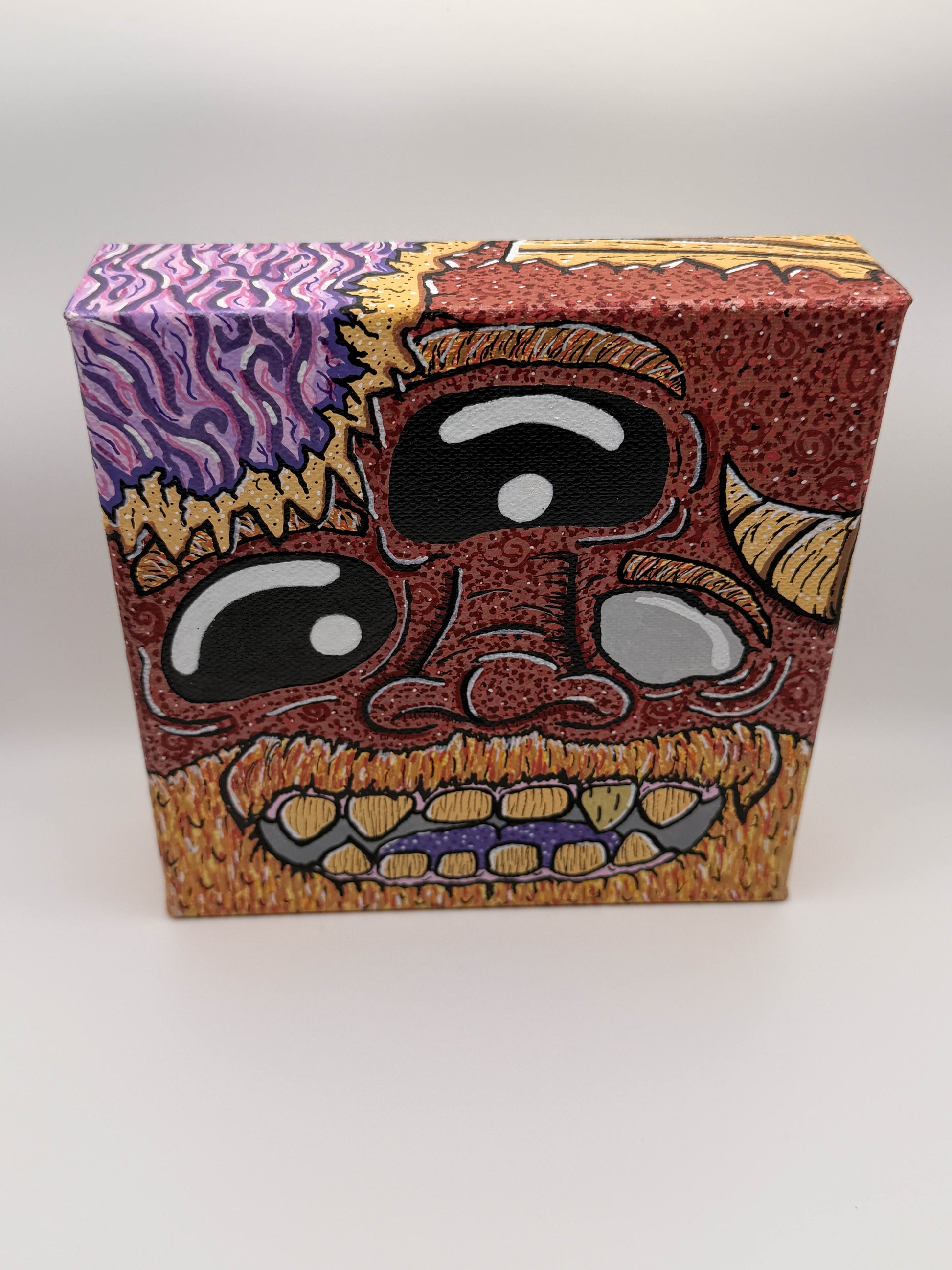 Top view of a red and gold monster character painted on a canvas block with purple brains on a white background.
