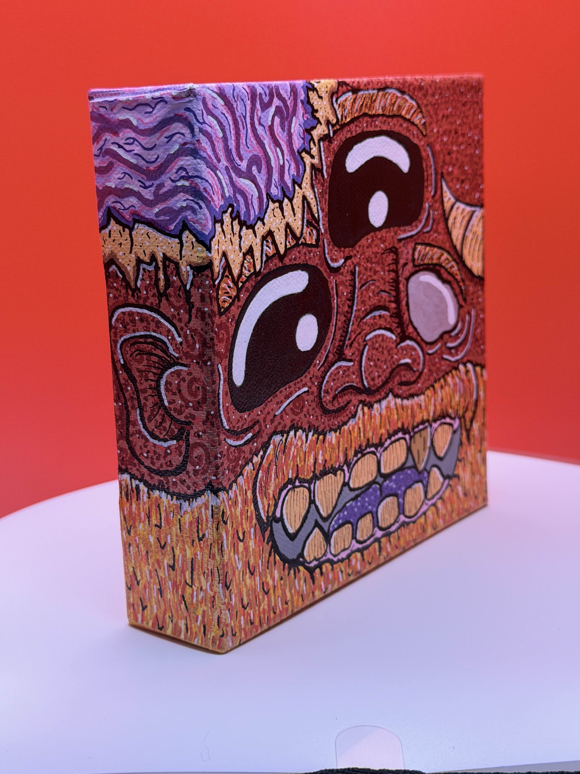 Side view of a red and gold monster character painted on a canvas block with purple brains on a red and white background.