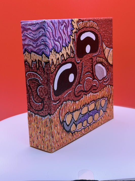 Side view of a red and gold monster character painted on a canvas block with purple brains on a red and white background.