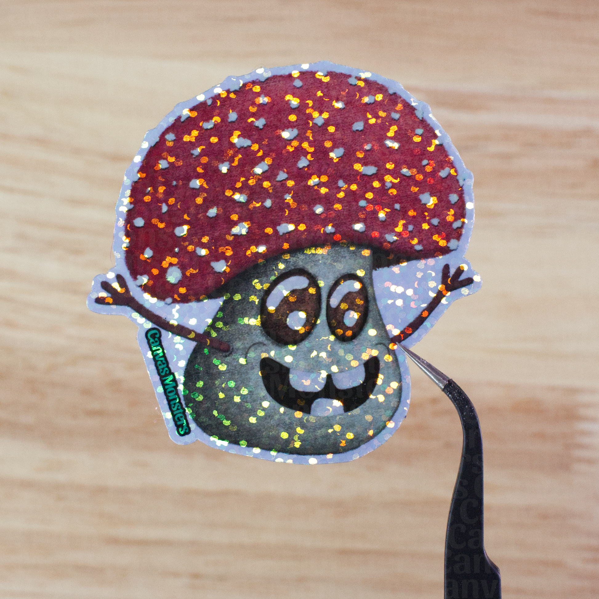 Glitter sticker of a cartoon mushroom held above a wooden surface