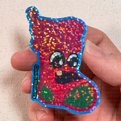 Colorful glitter sticker of a stocking character held by a hand on a beige fabric background