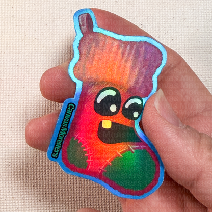 Colorful cartoon character sticker held between fingers on a beige background